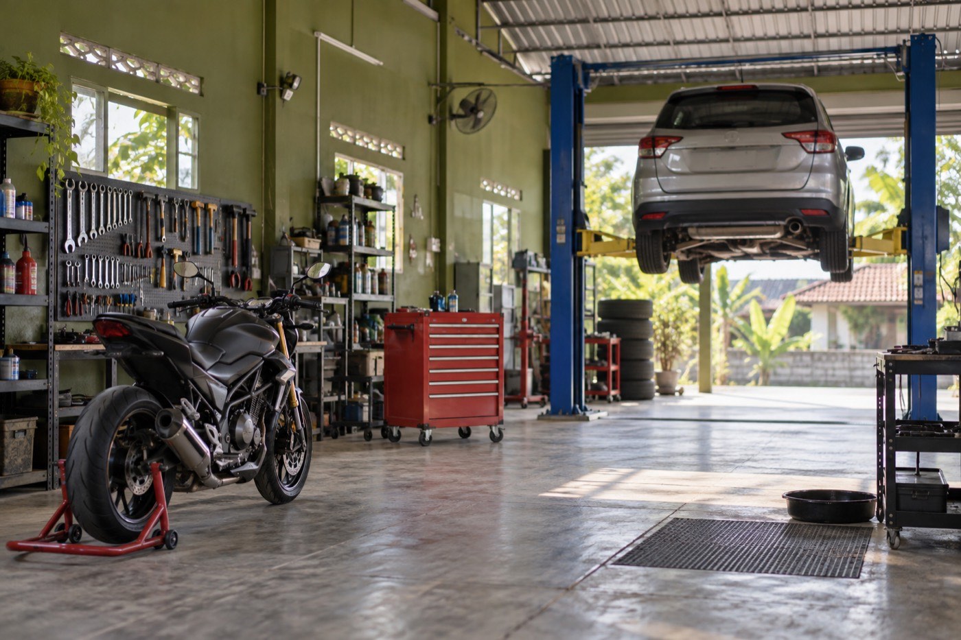 Bay kerja bengkel dengan lift mobil, lemari perkakas merah, dan motor di penyangga